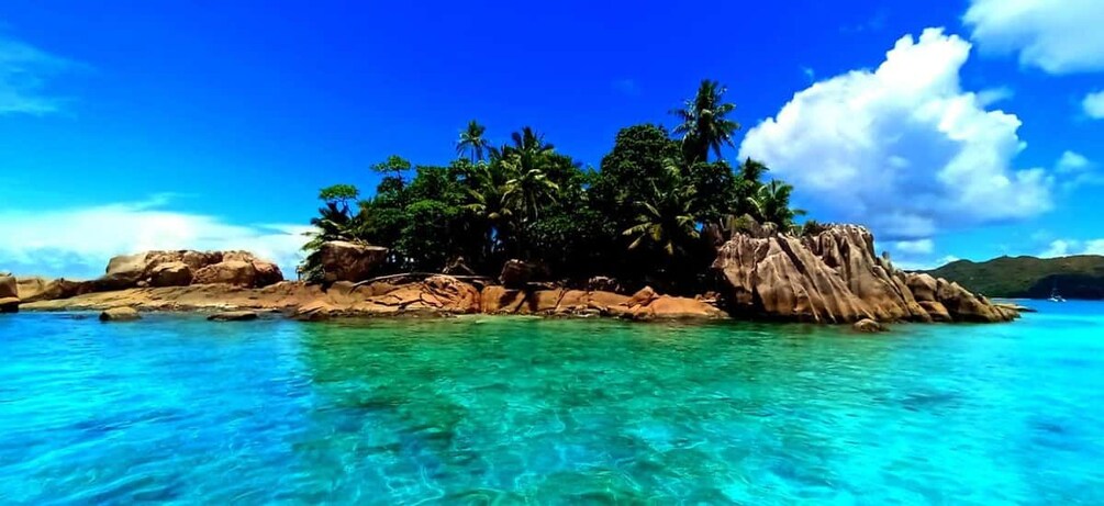A tropical island with clear turquoise waters, palm trees, and rocky outcrops. 1