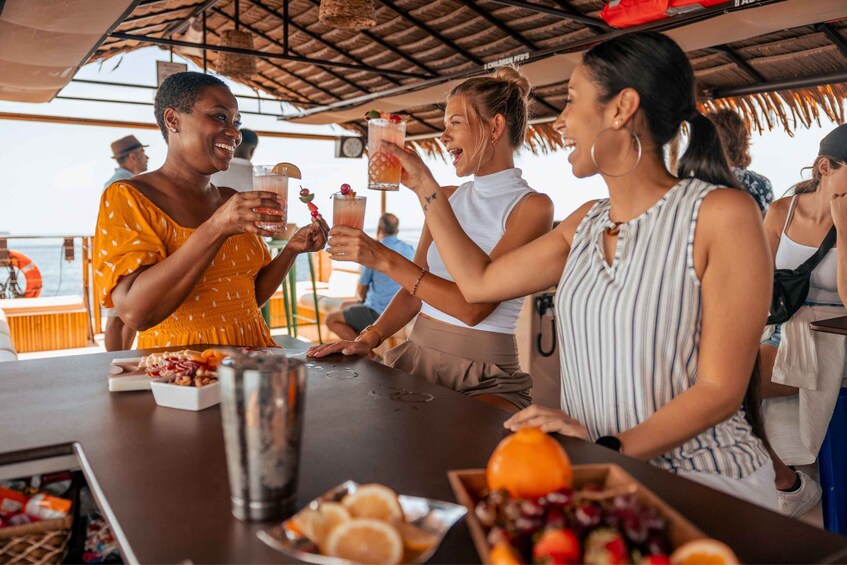 A group of people toasting with drinks at a bar with a thatched roof, overlooking a body of water. 5