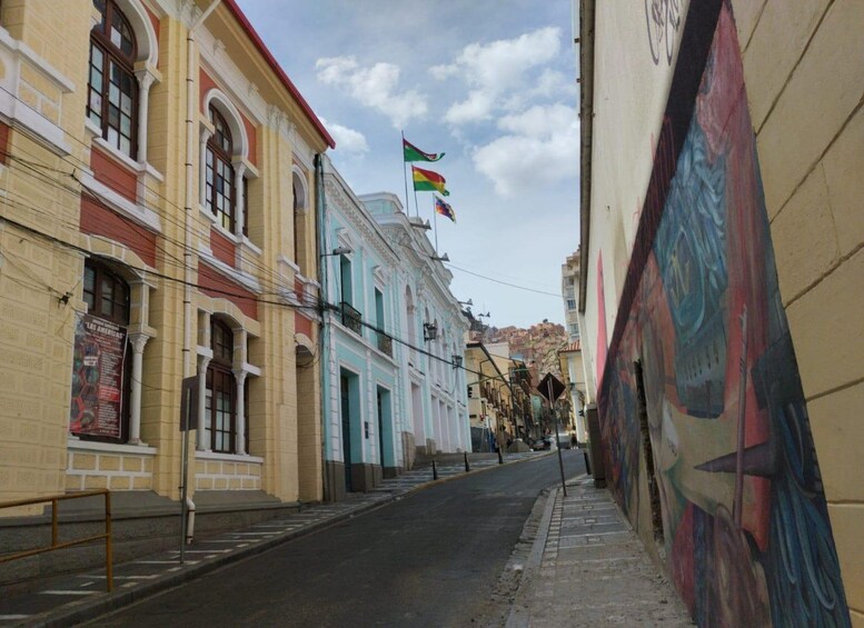 A narrow street lined with colorful buildings, a flag, and a mural. 2