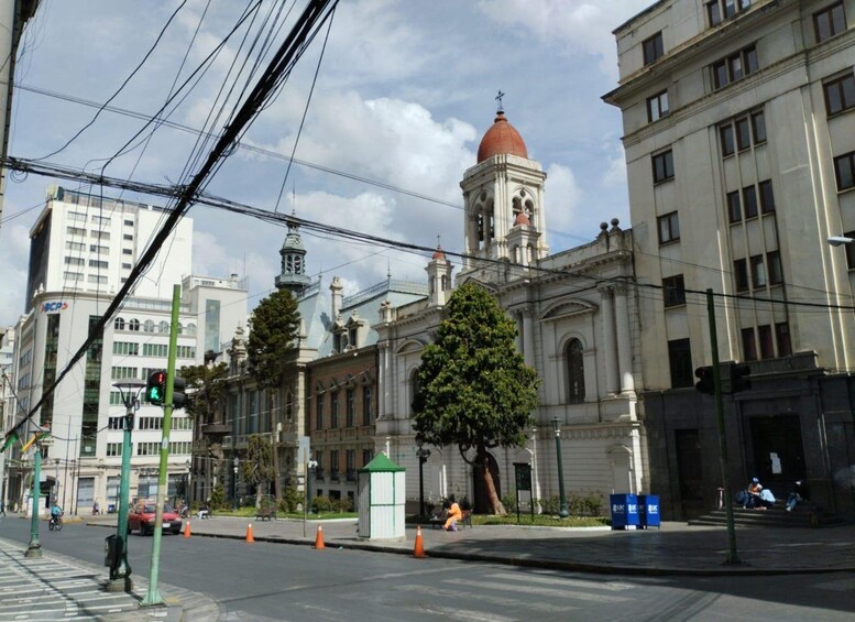 A street with a historic building featuring a red dome and bell tower, surrounded by modern buildings and power lines. 3