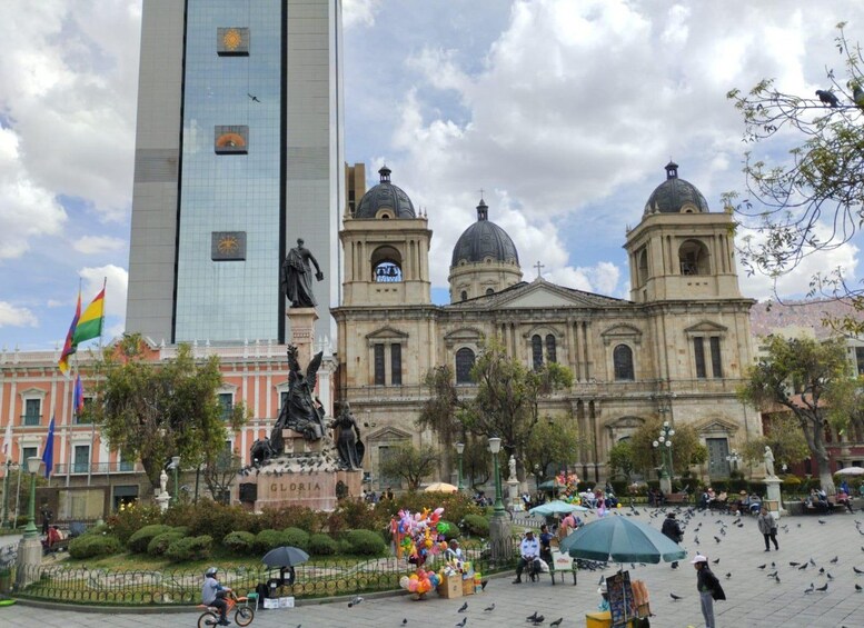A plaza with a large building, a statue, and a flag. 1