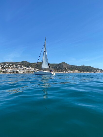 A sailboat on calm blue waters with a coastal town in the background. 3