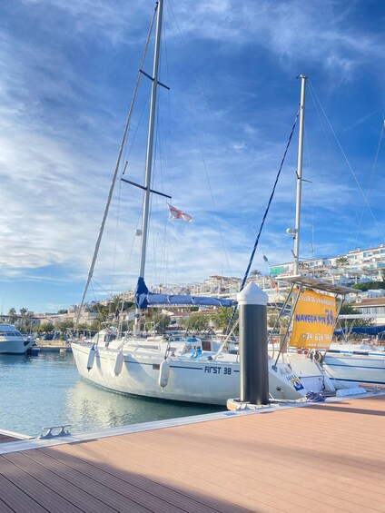 A sailboat docked at a marina with a clear sky and a cityscape in the background. 1
