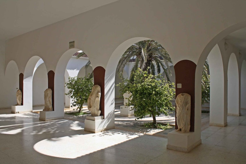 A series of white arches with classical statues and a palm tree in a courtyard. 3