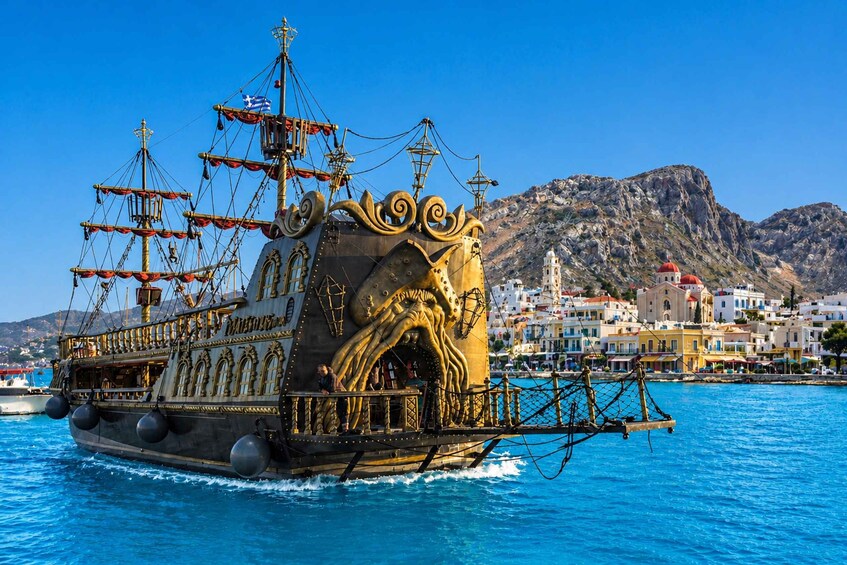 A large, ornate ship with multiple masts and sails, anchored in a harbor with a backdrop of colorful buildings and a mountainous landscape. 1