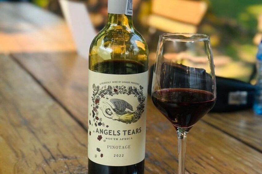A bottle of 2022 Angels Tears Pinotage wine and a glass of red wine on a wooden table. 2