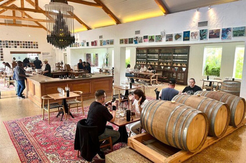 A wine tasting room with wooden barrels, a bar, and patrons seated at tables. 5