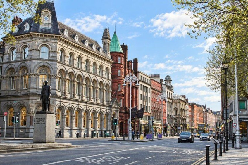 A street with historic buildings, a statue, and a green-roofed tower. 5
