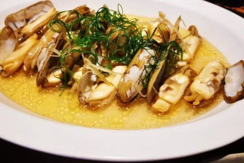 A dish of clams with green onions and a yellow sauce. 4