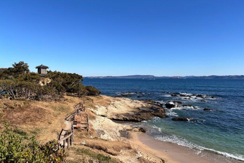 A coastal landscape with a wooden staircase leading to a traditional structure, a sandy beach, and the ocean. 4