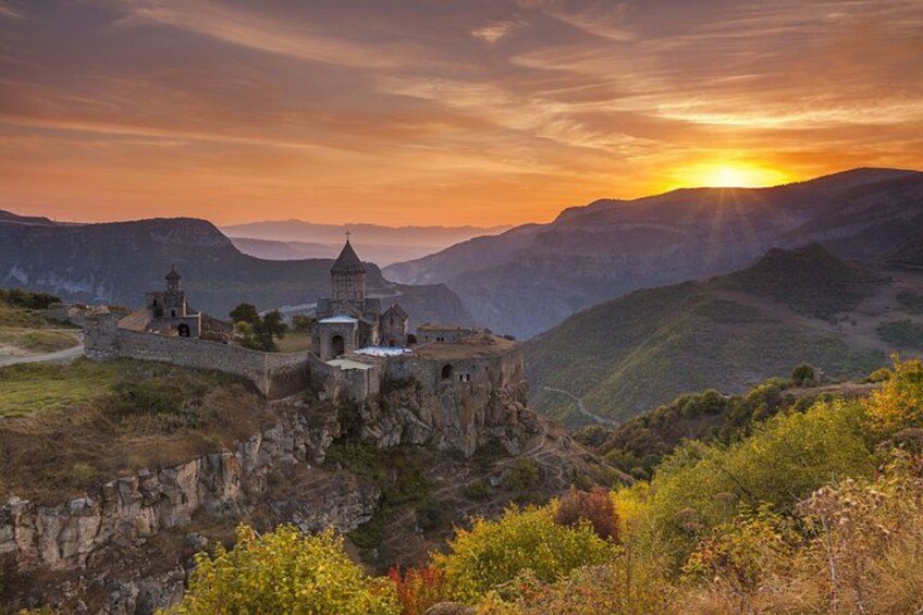A historic stone fortress with a bell tower, set against a backdrop of rolling hills and a sunset. 1