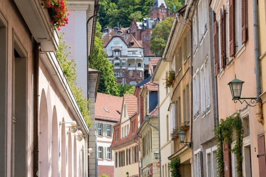 A narrow street with buildings on either side, some with flower boxes and greenery. 3