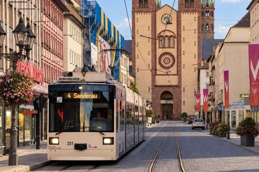 A tram with the number 4 and destination 'Sanderau' approaching a historic building with a clock tower. 4