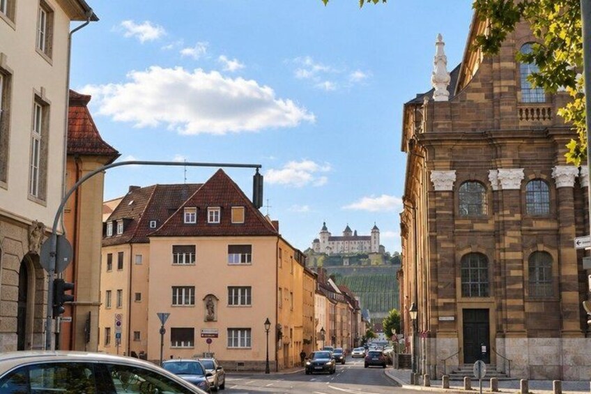 A street with buildings, cars, and a hill with a castle in the background. 2