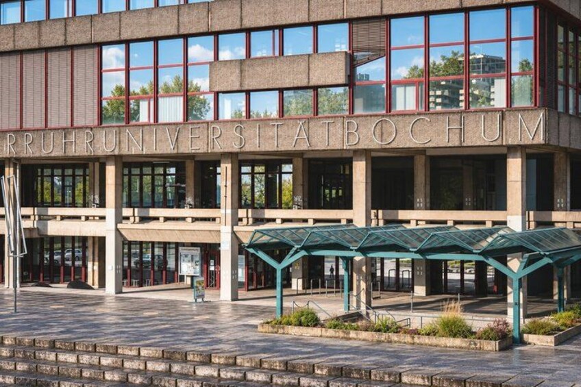 A modern building with the inscription 'RUHRUNIVERSITATBOCHUM' and a covered entrance area. 3