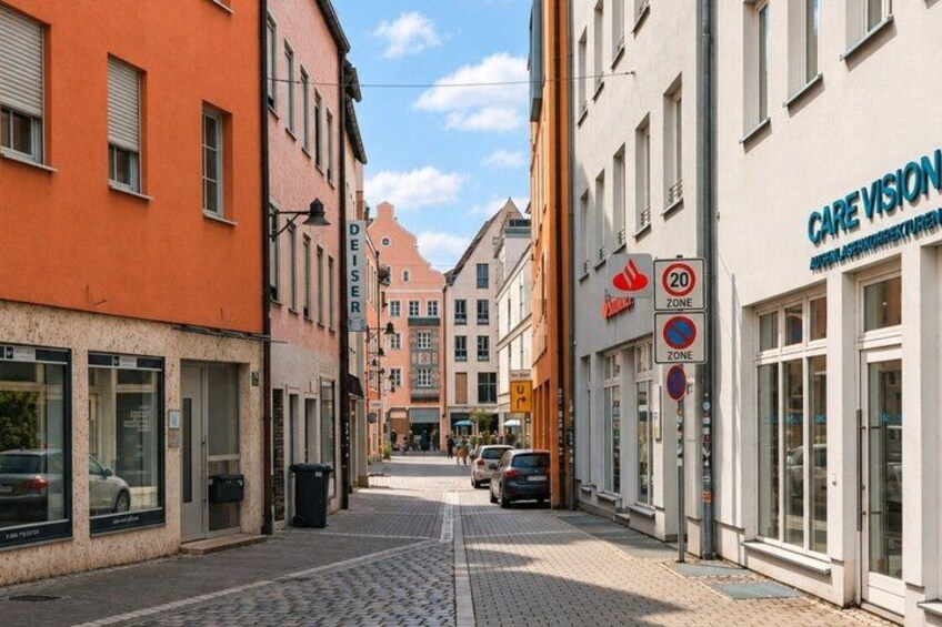 A cobblestone street lined with buildings, including a pharmacy and a care vision clinic. 4