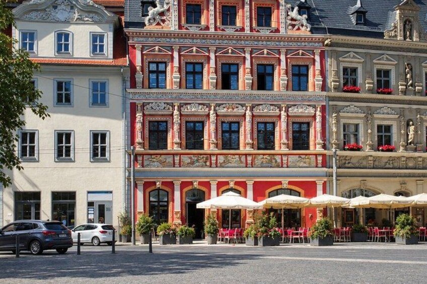 A row of colorful buildings with ornate facades, a street with parked cars, and outdoor seating at a cafe. 5