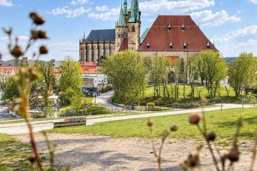 A historic church with a red roof and green spire, surrounded by trees and a paved path. 4