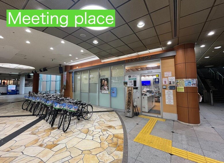 A public transportation hub with a meeting place sign, a bike rental station, and a ticket vending machine. 2