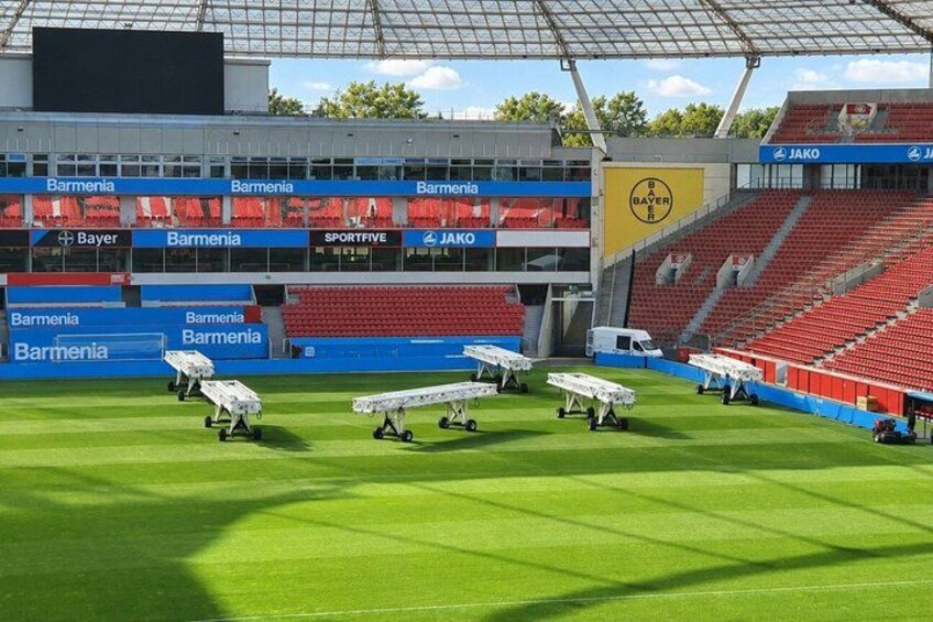 A stadium with empty red seats, solar panels on the field, and advertisements for Bayer and JAKO. 2