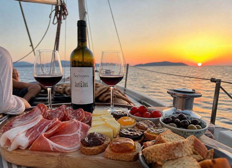 A sunset over the sea with a boat, a bottle of wine, glasses, and a charcuterie board with meats, cheeses, and olives. 1