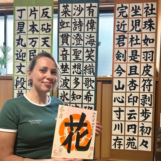 Une personne tenant un livre contenant des caractères chinois. On aperçoit en arrière-plan plusieurs banderoles verticales ornées de calligraphie chinoise. 2