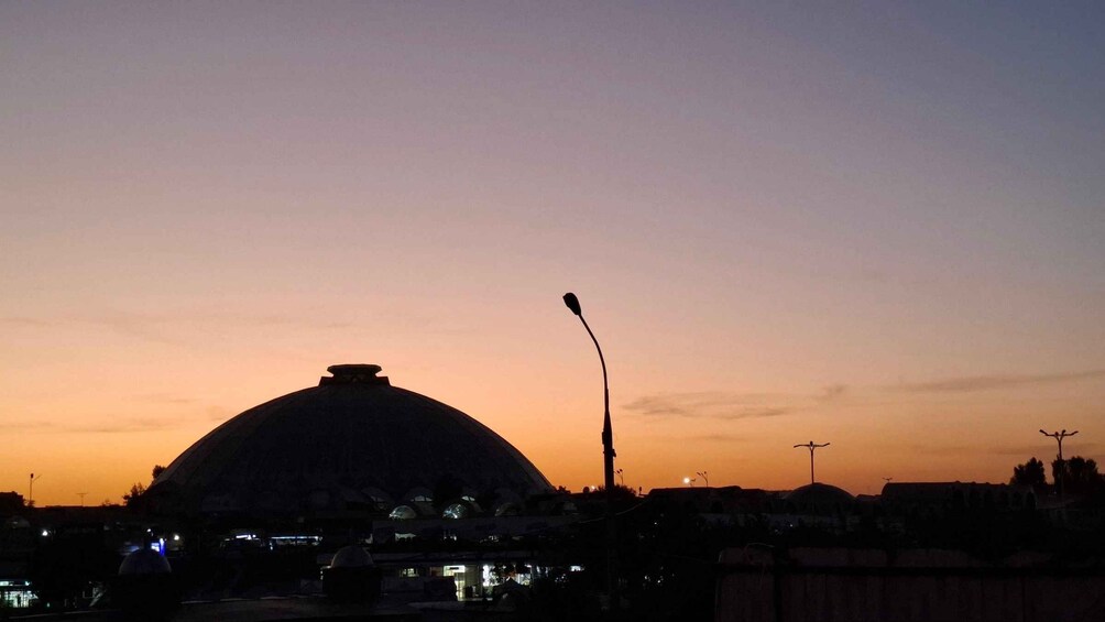 A large dome-shaped building silhouetted against a sunset sky, with a streetlight in the foreground. 4