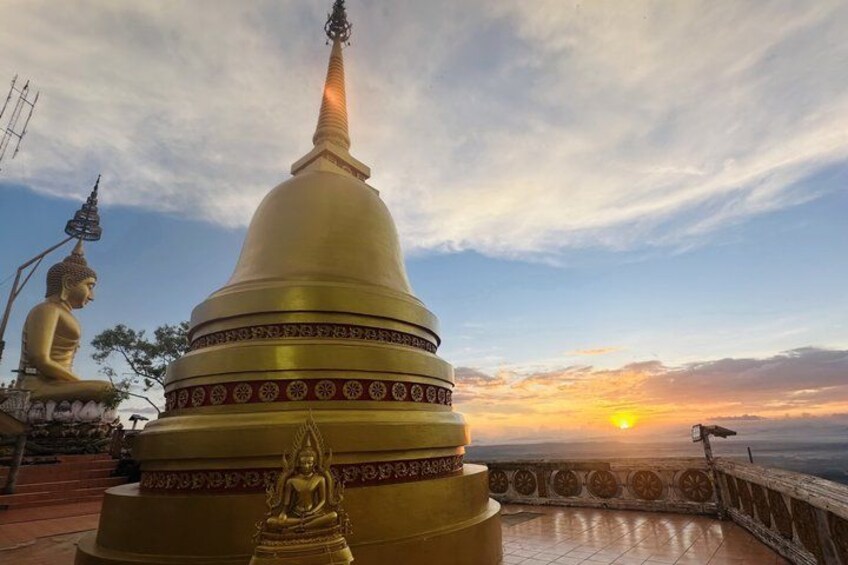 A golden stupa with intricate patterns, a seated Buddha statue, and a sunset in the background. 1