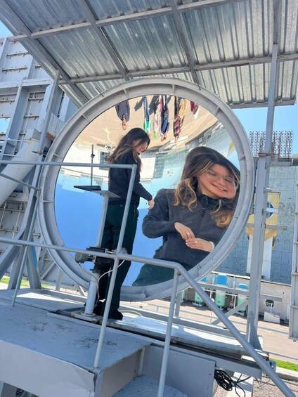 A circular viewing platform with metal railings, a clear sky, and a building with a blue facade in the background. 5