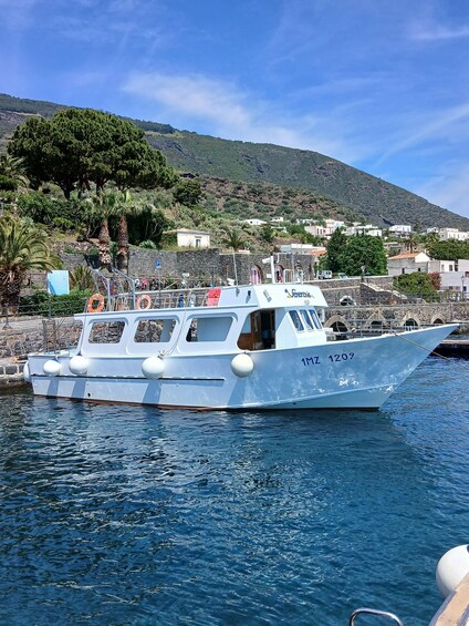 A boat docked at a harbor with a mountainous backdrop and coastal buildings. 1