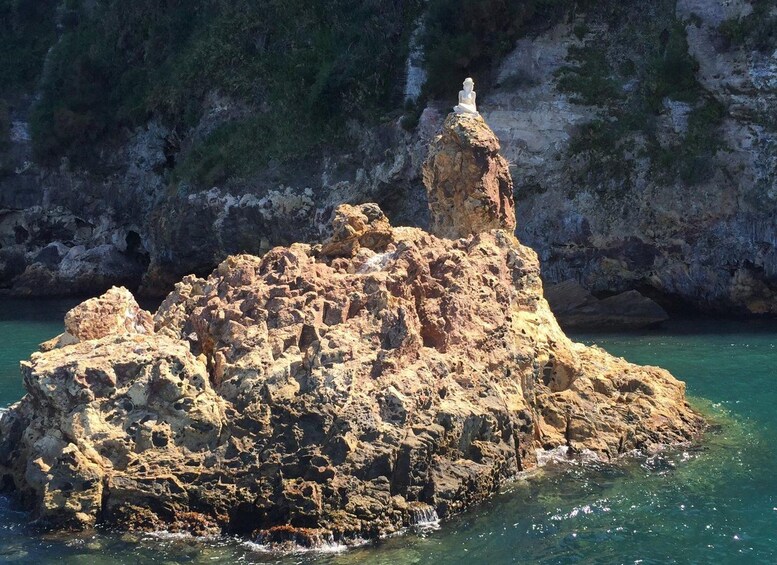 A rocky island with a statue on top, surrounded by clear blue water and a mountainous coastline. 2