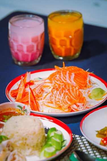 Et bord med forskellige retter, heriblandt en tallerken med revne gulerødder og en skål med ris. Der er også to glas med en pink og orange drik. 4