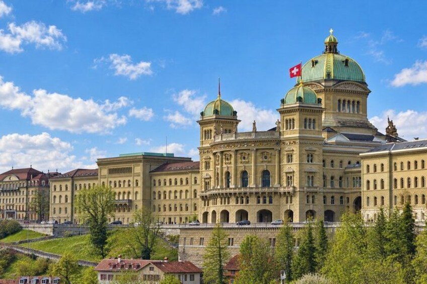 A large historic building with domed roofs and a flag, surrounded by trees and other buildings. 5