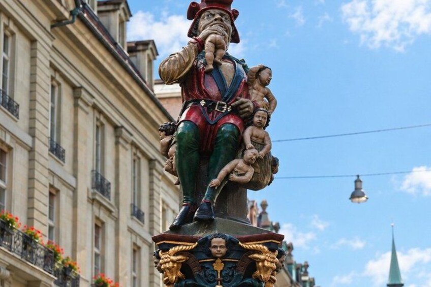 A statue of a man with children on his shoulders, set against a building with balconies and a clear sky. 3