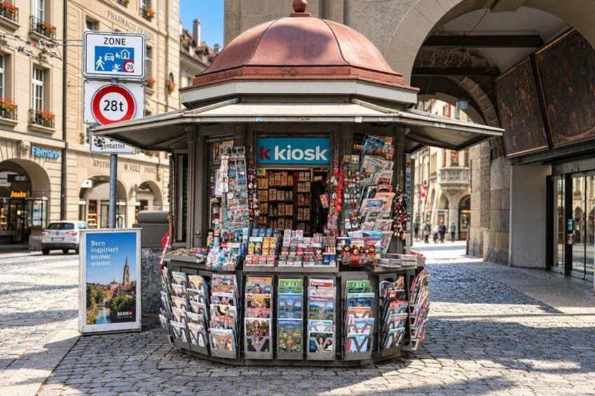 A kiosk with postcards and magazines, surrounded by cobblestone pavement and historic buildings. 4