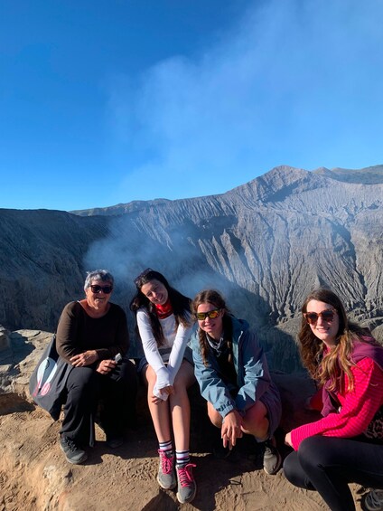 Four people sitting on a rocky outcrop with a mountainous landscape in the background. 3