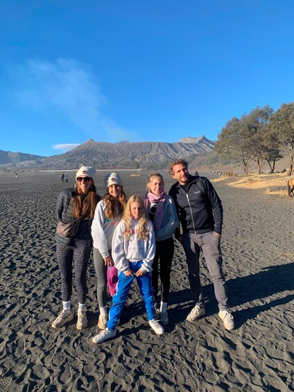 A group of people standing on a sandy beach with mountains in the background. 2