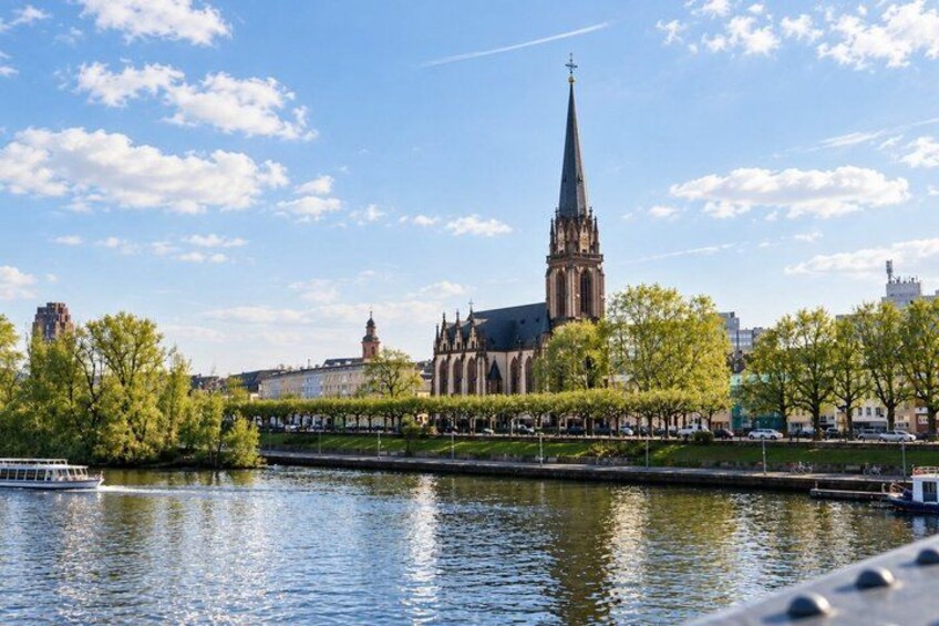 A river with a boat, a church with a tall spire, and trees along the riverbank. 2