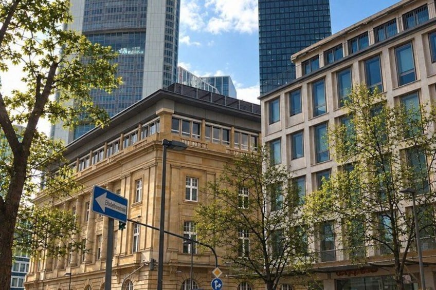 A historic building with a blue directional sign, surrounded by modern skyscrapers and trees. 4