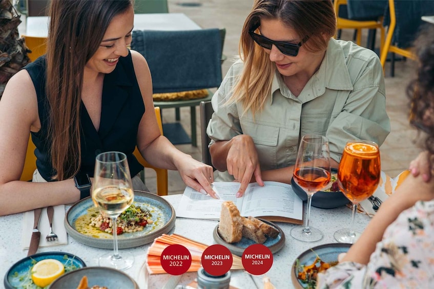 Two people dining at an outdoor restaurant with wine glasses and menus. 1