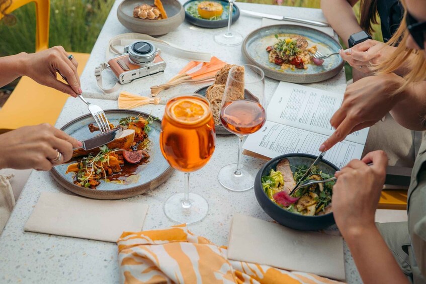 A group of people dining outdoors with various dishes, glasses of wine, and a menu. 5