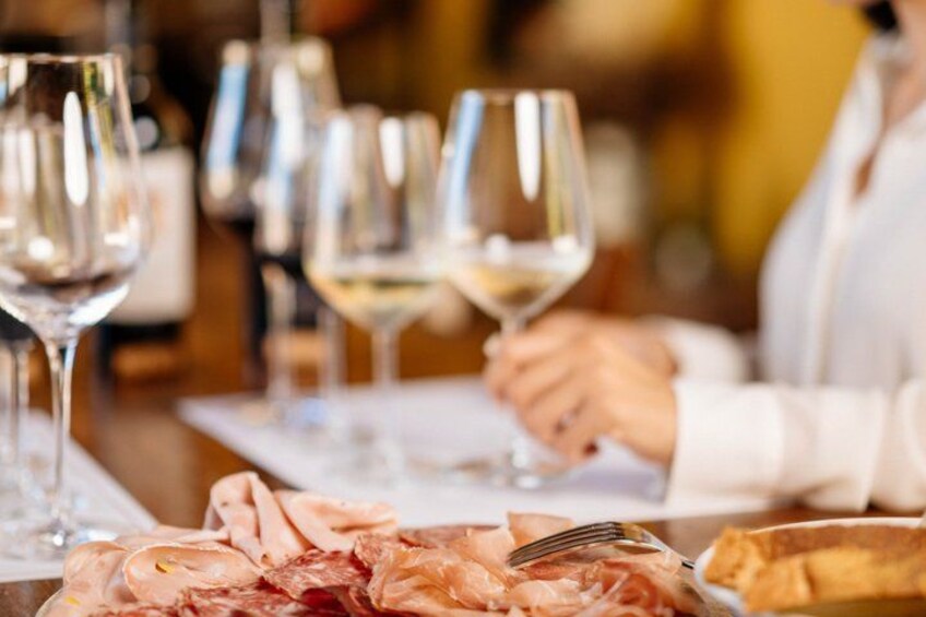 A dining table with a plate of sliced meats, a fork, and several wine glasses. 1