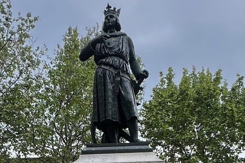 A statue of a historical figure with a crown, standing on a pedestal, surrounded by trees. 5
