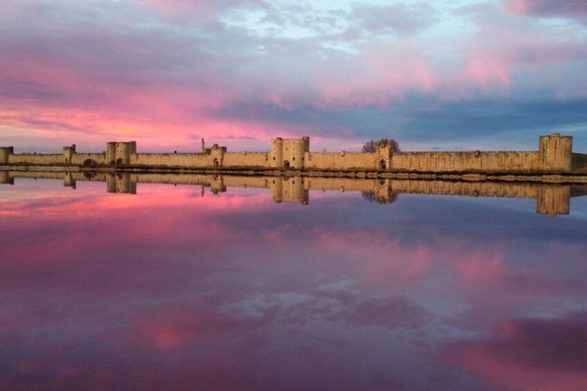 A castle wall reflecting in calm water under a colorful sky. 1