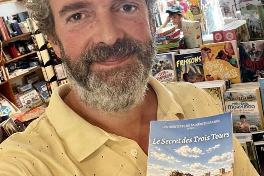 A person holding a book titled 'Le Secret des Trois Tours' in a bookstore with various other bookshelves in the background. 2