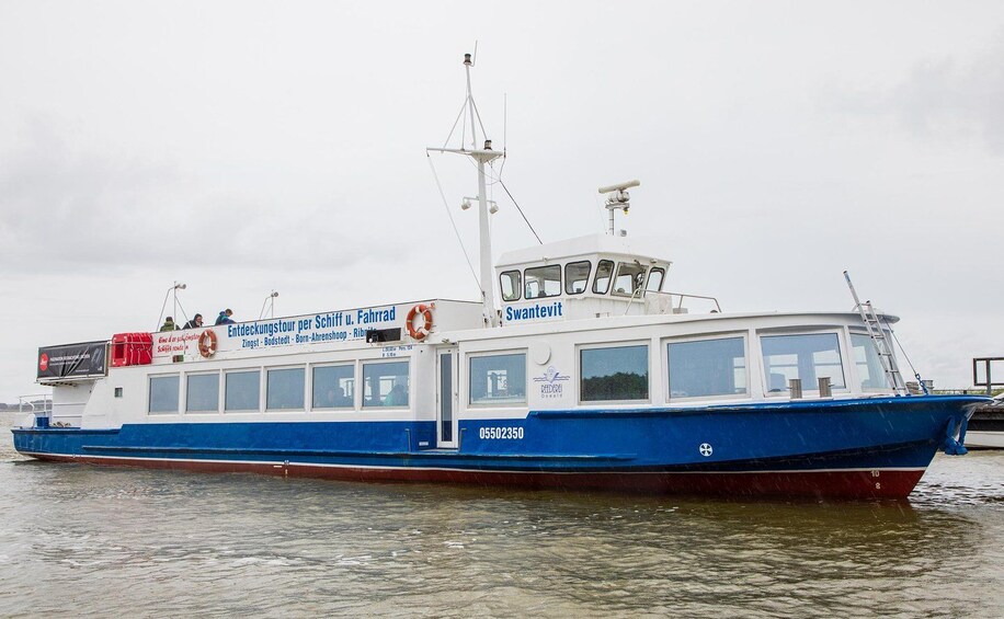 Un bateau bleu et blanc, portant l’inscription « Entdeckungstour per Schiff u. Fahrrad » sur sa coque, était amarré à un quai. 5