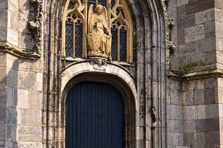 A stone building with a large arched entrance, a decorative window with a figure, and a stone facade. 2