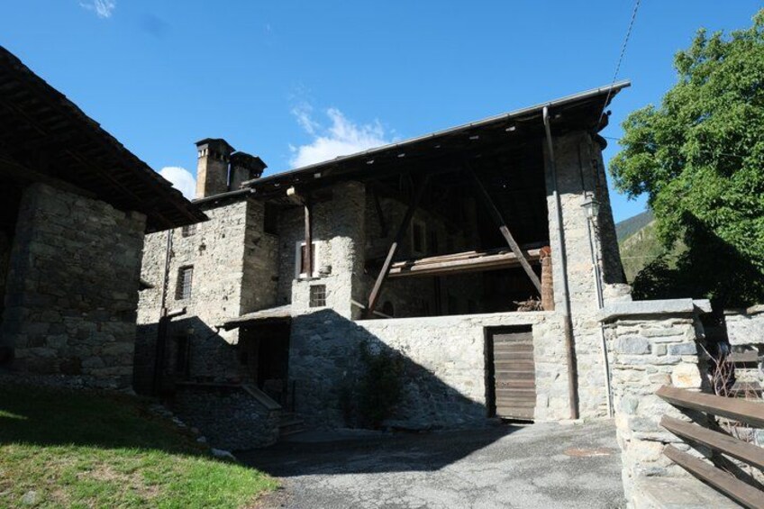 A stone building with a wooden beam structure, a stone staircase, and a grassy area. 4