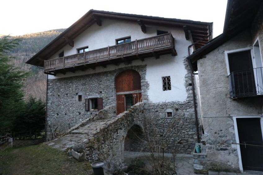 A stone building with a wooden door and balcony, surrounded by a mountainous landscape. 5