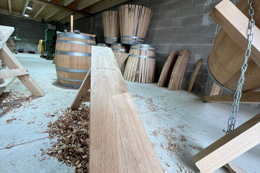 A woodworking workshop with wooden planks, a workbench, and large wooden barrels. 4